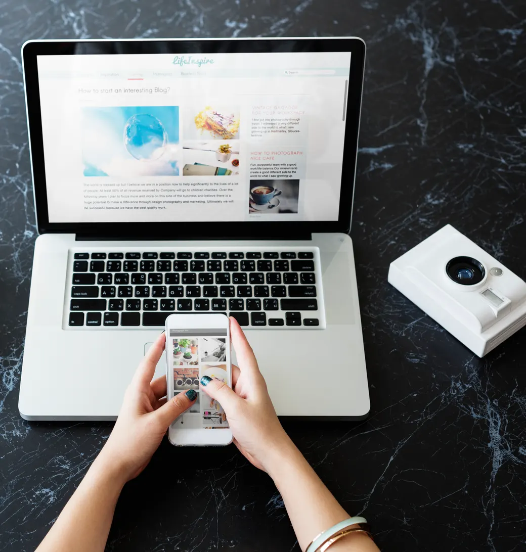 Hands browsing a social media feed on a phone beside a laptop